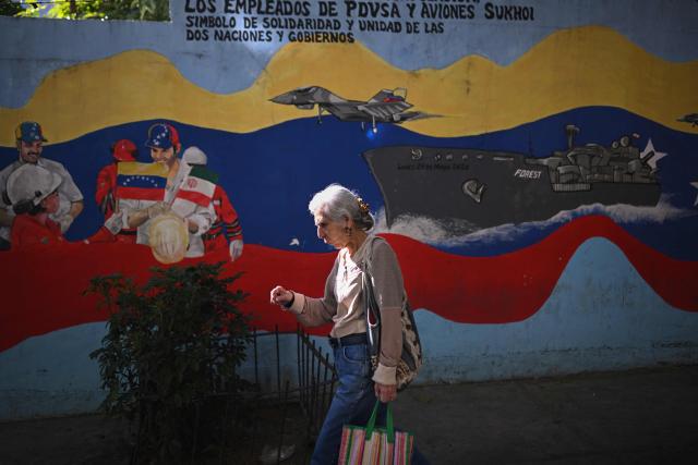 A woman walks past a mural of Venezuela's warship and warplanes on a street in Caracas on December 26, 2025. (Photo by Federico PARRA / AFP)
