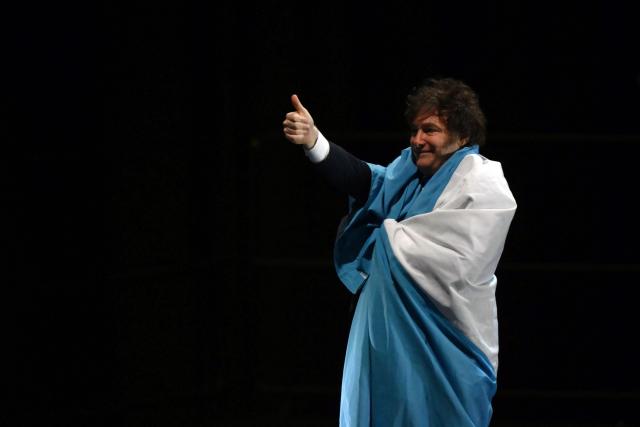 (FILES) Argentina's President Javier Milei gives a thumbs-up while wrapped in the Argentine flag during the launch of his new book, "The Making of the Miracle," at the Movistar Arena in Buenos Aires on October 6, 2025. On December 26, 2025, the Argentine Senate approved Javier Milei's first budget proposal, which had previously received approval from deputies, providing a boost for the second half of his term after two years of governing with outdated figures. (Photo by Luis ROBAYO / AFP)