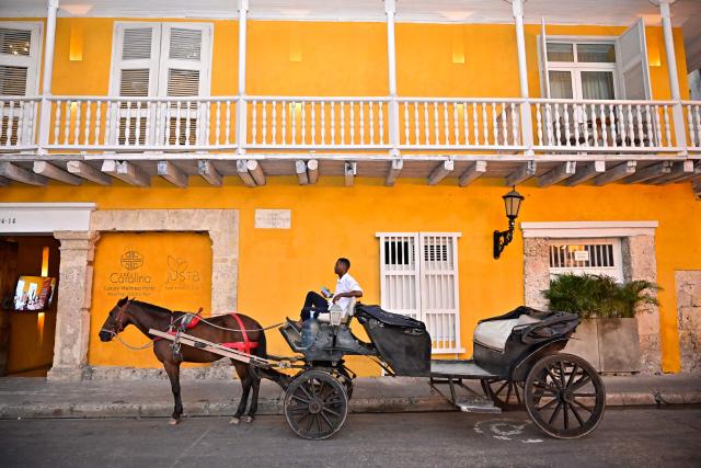 A coachman in his horse-drawn carriage waits for customers at the historic center of Cartagena, Colombia, on December 26, 2025. Traditional horse-drawn carriages will be banned starting December 29, 2025, in Cartagena, a tourist jewel of Colombia, the local mayor announced on December 26. (Photo by Manuel PEDRAZA / AFP)