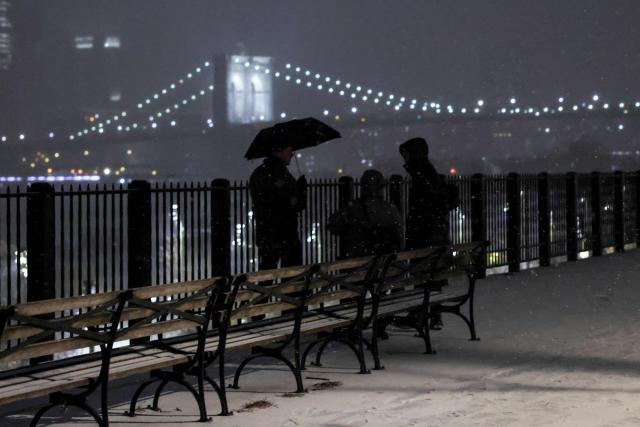 People chat during a snowfall, backdropped by the Brooklyn Brige, on December 26, 2025 in New York City. (Photo by ANGELA WEISS / AFP)