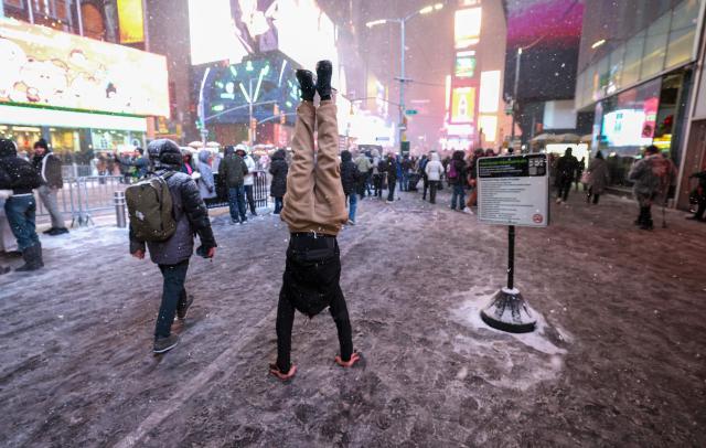 A man walks on his hands during a snowfall in Times Square on December 26, 2025, in New York City. New York, the US largest city, was bracing for up to 10 inches (25 centimeters) of snow overnight, the most in four years. (Photo by TIMOTHY A. CLARY / AFP)