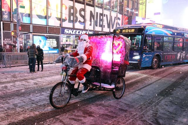 A pedicab tour guide, dressed in a Santa Claus costume, rides during a snowfall in Times Square on December 26, 2025, in New York City. New York, the US largest city, was bracing for up to 10 inches (25 centimeters) of snow overnight, the most in four years. (Photo by TIMOTHY A. CLARY / AFP)