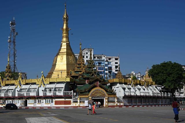 People walk past the Sule Pagoda in Yangon on December 27, 2025, a day before the start of Myanmar's general election. (Photo by Nhac NGUYEN / AFP)