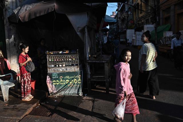 People walk in a street in Yangon on December 27, 2025, a day before the start of Myanmar's general election. (Photo by Lillian SUWANRUMPHA / AFP)