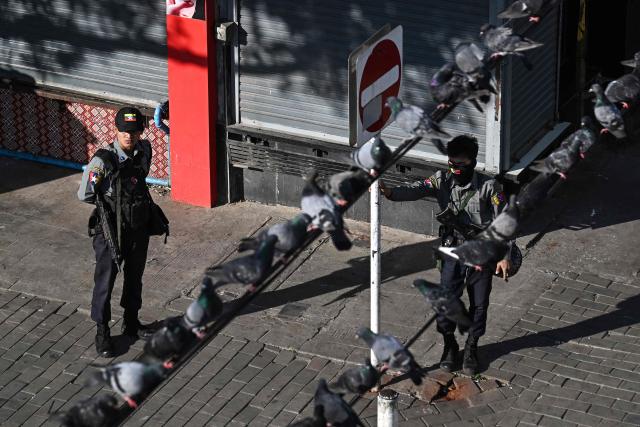 Police officers stand on a street corner as pigeons sit on a electricity cable in Yangon on December 27, 2025, a day before the start of Myanmar's general election. (Photo by Lillian SUWANRUMPHA / AFP)