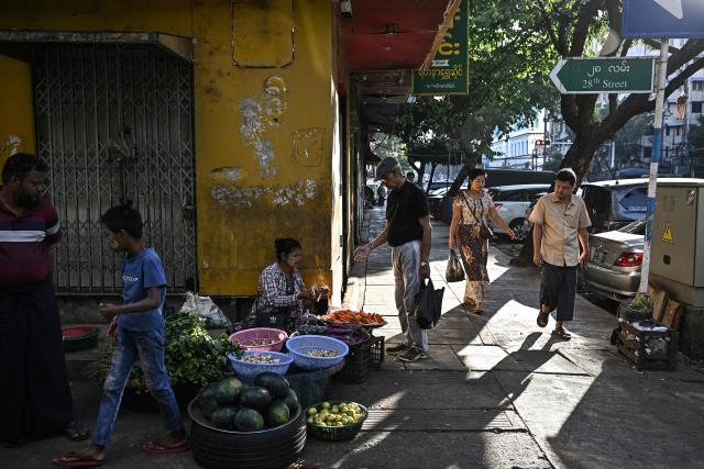 A vendor hands change to a customer at a street market in Yangon on December 27, 2025, a day before the start of Myanmar's general election. (Photo by Lillian SUWANRUMPHA / AFP)