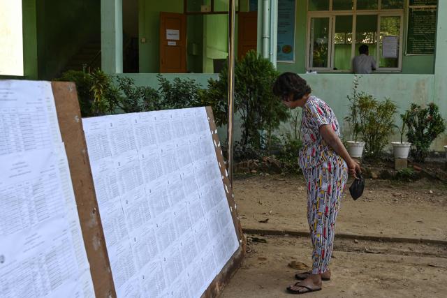A woman checks name lists at a polling station a day before the start of Myanmar's general election in Yangon on December 27, 2025. (Photo by NHAC NGUYEN / AFP)