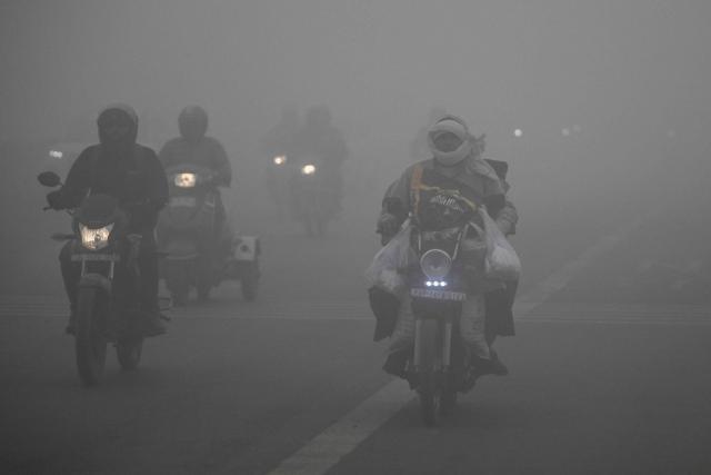Commuters ride along a street amid dense smog in New Delhi on December 27, 2025. (Photo by Arun SANKAR / AFP)
