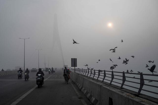 Commuters ride along the Signature Bridge over Yamuna river amid dense smog in New Delhi on December 27, 2025. (Photo by Arun SANKAR / AFP)