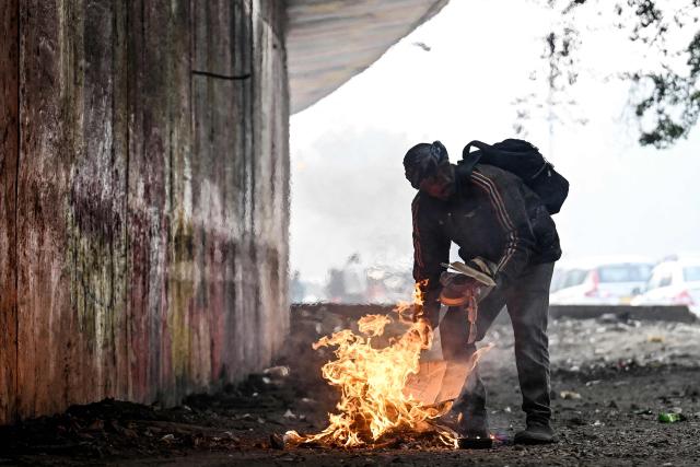 A man lights a bonfire on a cold winter morning in New Delhi on December 27, 2025. (Photo by Arun SANKAR / AFP)