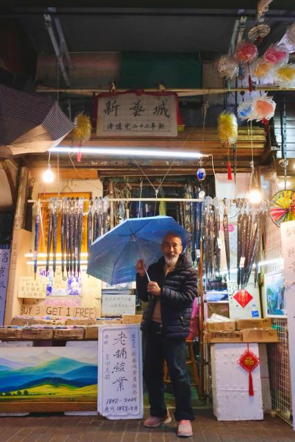 Yau Yiu-wai, 73, one of the few remaining umbrella repairmen in Hong Kong, poses with an umbrella in Hong Kong’s Sham Shui Po district on December 26, 2025. Scores of residents flocked to a cramped shop in Hong Kong's old district to bid farewell to the city's "king of umbrellas", who is retiring after spending decades repairing umbrellas at his family business. (Photo by Tommy WANG / AFP) / To go with 'HONG KONG-CHINA-SOCIAL, REPORTAGE' by Tommy Wang