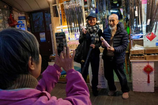 Yau Yiu-wai (R), 73, one of the few remaining umbrella repairmen in Hong Kong, poses with a customer in Hong Kong’s Sham Shui Po district on December 26, 2025. Scores of residents flocked to a cramped shop in Hong Kong's old district to bid farewell to the city's "king of umbrellas", who is retiring after spending decades repairing umbrellas at his family business. (Photo by Tommy WANG / AFP) / To go with 'HONG KONG-CHINA-SOCIAL, REPORTAGE' by Tommy Wang