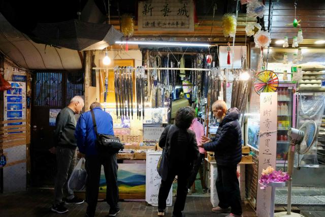 Yau Yiu-wai (R), 73, one of the few remaining umbrella repairmen in Hong Kong, talks to customers in Hong Kong’s Sham Shui Po district on December 26, 2025. Scores of residents flocked to a cramped shop in Hong Kong's old district to bid farewell to the city's "king of umbrellas", who is retiring after spending decades repairing umbrellas at his family business. (Photo by Tommy WANG / AFP) / To go with 'HONG KONG-CHINA-SOCIAL, REPORTAGE' by Tommy Wang
