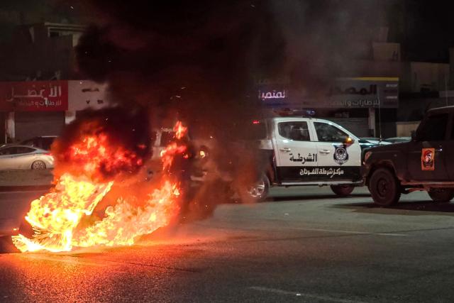 Police vehicles are parked near burning tires as protesters blocked a key intersection of the capital with calls to bring down the government, in the Libyan capital Tripoli late on December 26, 2025. (Photo by Mahmud TURKIA / AFP)