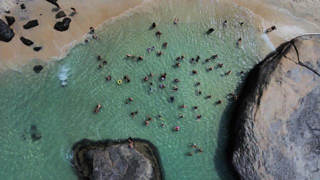 An aerial view shows people enjoying Grumari Beach, located in southwest Rio de Janeiro, Brazil, on December 27, 2025. (Photo by TERCIO TEIXEIRA / AFP)