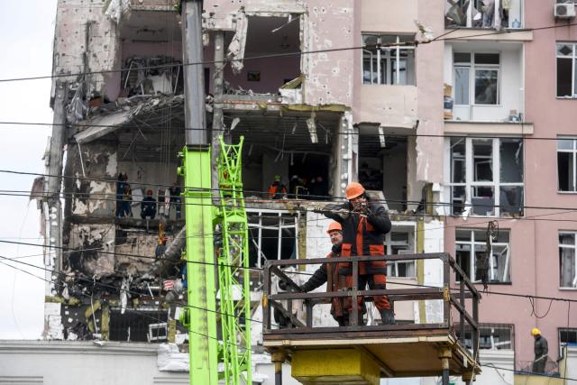 Workers repare cables in front of a damaged residential building following Russian drones and missiles attack in Kyiv, on December 27, 2025, amid the Russian invasion in Ukraine. Russia pummelled Ukraine's capital with drones and missiles on December 27, killing a woman and cutting power to hundreds of thousands, ahead of the latest talks between the presidents of Ukraine and the US. (Photo by VLADYSLAV MUSIENKO / AFP)