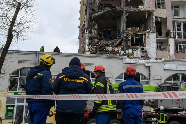 Ukrainian rescuers stand in front of a damaged residential building following Russian drones and missiles attack in Kyiv, on December 27, 2025, amid the Russian invasion in Ukraine. Russia pummelled Ukraine's capital with drones and missiles on December 27, killing a woman and cutting power to hundreds of thousands, ahead of the latest talks between the presidents of Ukraine and the US. (Photo by VLADYSLAV MUSIENKO / AFP)