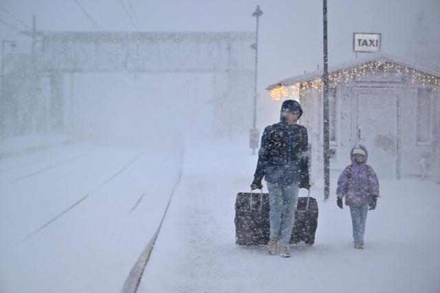 A woman and child make their way with their luggage at the train station in Are as storm Johannes moves in over northern Sweden causing cancelled departures on December 27, 2025. (Photo by Pontus LUNDAHL / various sources / AFP) / Sweden OUT