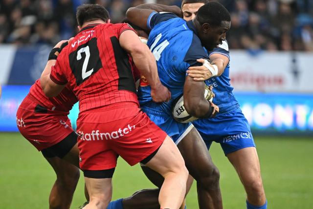 Castres' Cameroonian wing Christian Ambadiang (2nd R) breaks through a tackle during the French Top 14 rugby union match between Castres Olympique and Lyon Olympique Universitaire Rugby (LOU) at Stade Pierre Fabre in Castres, southern France, on December 27, 2025. (Photo by Matthieu RONDEL / AFP)