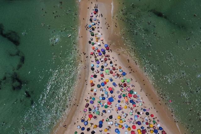 An aerial view shows people enjoying Recreio dos Bandeirantes beach, in the southwest zone, as large groups of broadband anchovies (Anchoviella lepidentostole) are seen in the ocean in Rio de Janeiro, Brazil, on December 27, 2025. (Photo by TERCIO TEIXEIRA / AFP)