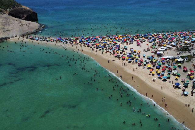 An aerial view shows people enjoying Recreio dos Bandeirantes beach, located in southwest Rio de Janeiro, Brazil on December 27, 2025. (Photo by TERCIO TEIXEIRA / AFP)