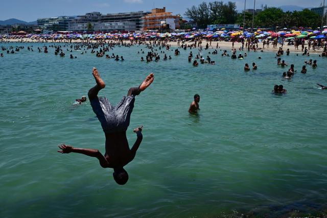 A young man jumps from a rock into the sea at Recreio dos Bandeirantes beach, in the southwest zone of Rio de Janeiro, Brazil on December 27, 2025. (Photo by TERCIO TEIXEIRA / AFP)