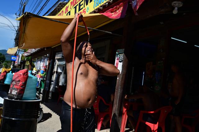 A man takes a shower to cool off from the high temperatures on a street in the Guaratiba neighborhood of Rio de Janeiro, Brazil on December 27, 2025. (Photo by Tercio TEIXEIRA / AFP)
