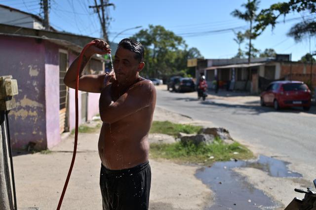 A man takes a shower to cool off from the high temperatures on a street in the Guaratiba neighborhood of Rio de Janeiro, Brazil on December 27, 2025. (Photo by TERCIO TEIXEIRA / AFP)