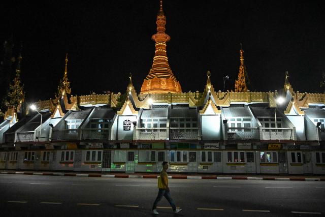 A man walks in front of the Sule Pagoda during the first phase of Myanmar's general election in Yangon on December 28, 2025. Voting begins in Myanmar's heavily restricted polls, with the ruling junta touting the exercise as a return to democracy five years after it ousted the last elected government, triggering civil war. (Photo by NHAC NGUYEN / AFP)