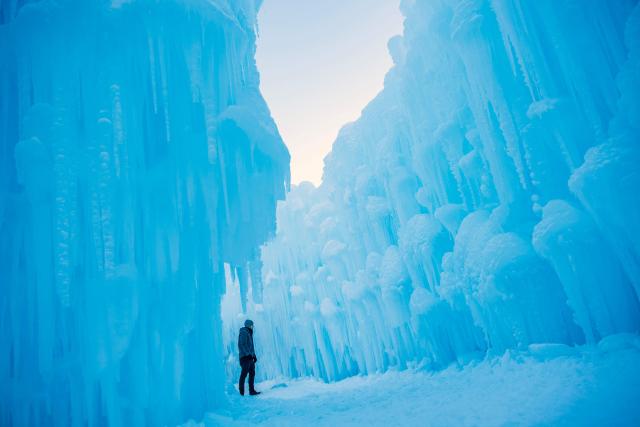 A person explores an ice path of the Ice Castles during the opening day in North Woodstock, New Hampshire on December 27, 2025. Brent Christensen crafted his first icy creation in the front yard of his home to bring happiness and joy to his children, and since 2011, Ice Castles has been dedicated to creating a world of ice caves, frozen waterfalls, and glaciers formed into archways, caverns, slides, and tunnels. (Photo by Joseph Prezioso / AFP)