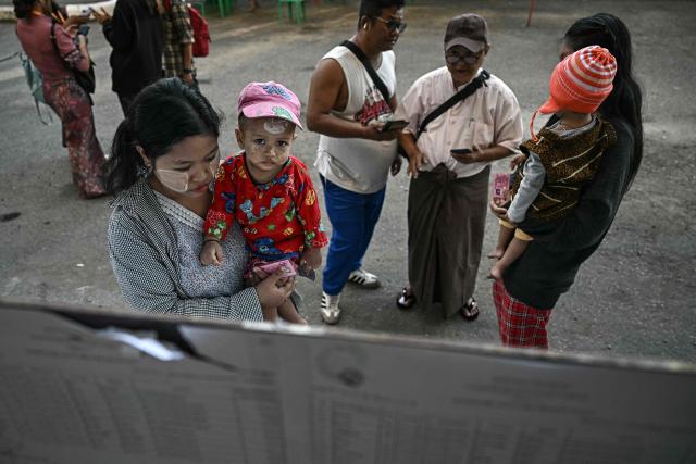 A voter (L) look for her name on the registry at a polling station during the first phase of Myanmar's general election in Yangon on December 28, 2025. Polling opened in Myanmar's heavily restricted junta-run elections, beginning a month-long vote democracy watchdogs describe as a rebranding of military rule. (Photo by Lillian SUWANRUMPHA / AFP)