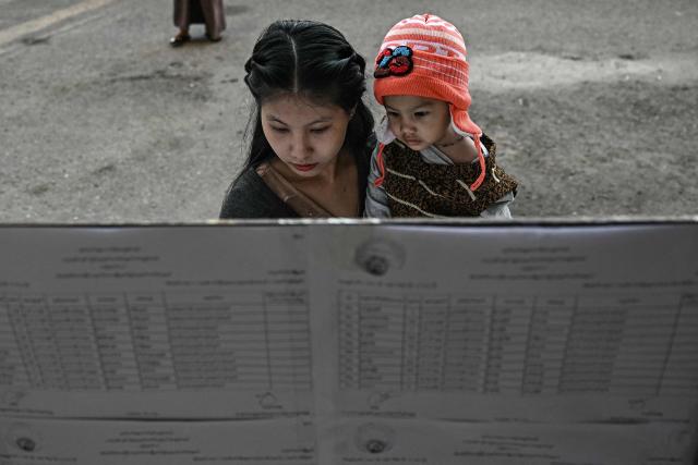 A voter (L) look for her name on the registry at a polling station during the first phase of Myanmar's general election in Yangon on December 28, 2025. Polling opened in Myanmar's heavily restricted junta-run elections, beginning a month-long vote democracy watchdogs describe as a rebranding of military rule. (Photo by Lillian SUWANRUMPHA / AFP)