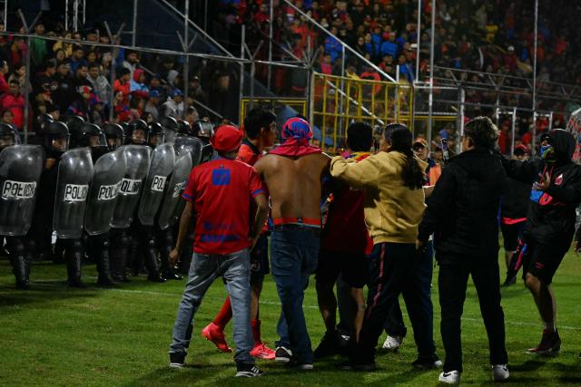 Fans of Municipal clash with riot police offices after the Guatemalan Apertura tournament final second-leg football match between Municipal and Antigua at El Trebol Stadium in Guatemala City on December 27, 2025. (Photo by JOHAN ORDONEZ / AFP)