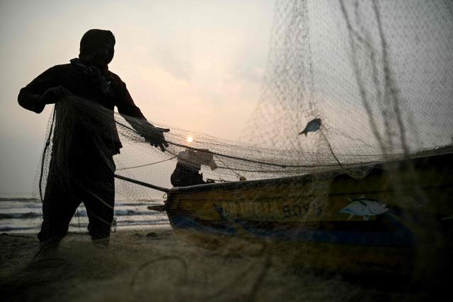 A fisherman cleans his net after his early morning catch at the Marina beach in Chennai on December 28, 2025. (Photo by R. Satish BABU / AFP)