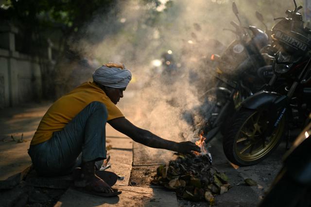 A man lights a bonfire on a cold winter morning in Chennai on December 28, 2025. (Photo by R. Satish BABU / AFP)