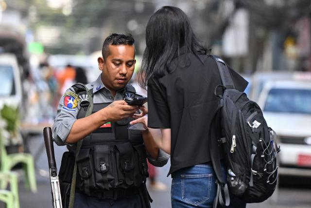 A police officer controls the pass of a journalist at the entrance of a polling station during the first phase of Myanmar's general election in Yangon on December 28, 2025. (Photo by NHAC NGUYEN / AFP)