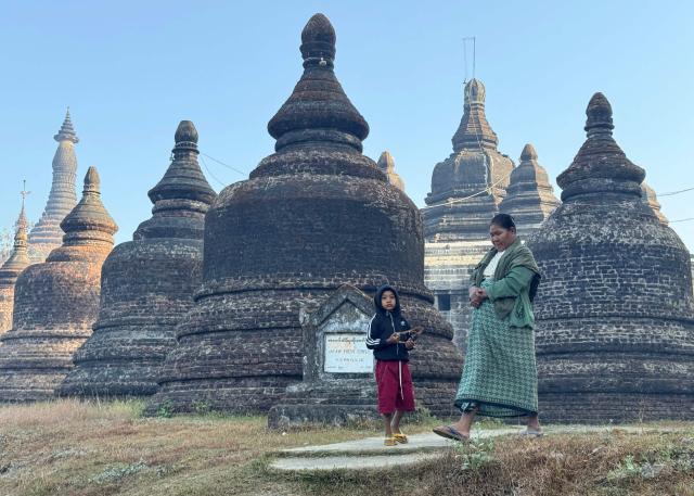 A woman and a child walk past the Andaw Thein temple in Mrauk U, in Myanmar's western Rakhine state on December 28, 2025. Myanmar's civil war has seen the military lose swathes of the country to rebel forces -- a mix of pro-democracy guerillas and ethnic minority armies which have long resisted central rule -- and the vote will not take place in the areas they control. (Photo by AFP)