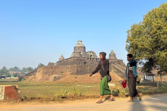People walk on a road past the Htukkant Thein temple in Mrauk U, in Myanmar's western Rakhine state on December 28, 2025. Myanmar's civil war has seen the military lose swathes of the country to rebel forces -- a mix of pro-democracy guerillas and ethnic minority armies which have long resisted central rule -- and the vote will not take place in the areas they control. (Photo by AFP)