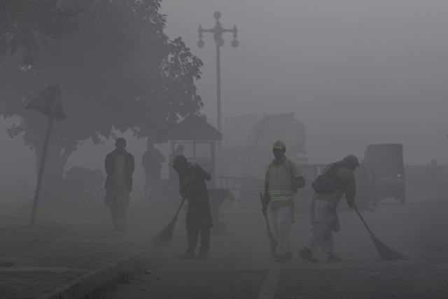 Workers sweep a street amid dense smog in Lahore on December 28, 2025. (Photo by Arif ALI / AFP)