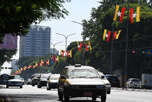 Vehicles drive on a road under Myanmar's flags displayed for the country's general election in Yangon on December 28, 2025. (Photo by NHAC NGUYEN / AFP)
