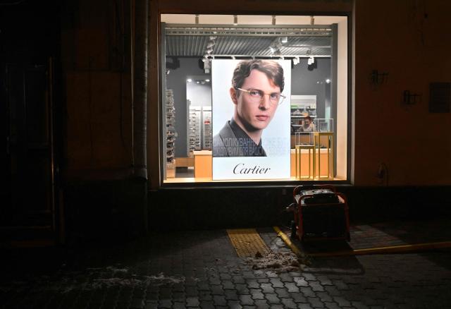 This photograph shows a power generator working outside a glasses store in a non-illuminated street during a power outage in Kyiv on December 27, 2025, following Russian missile and drone attacks on Ukrainian energy infrastructure amid the Russian invasion of Ukraine. (Photo by Sergei SUPINSKY / AFP)