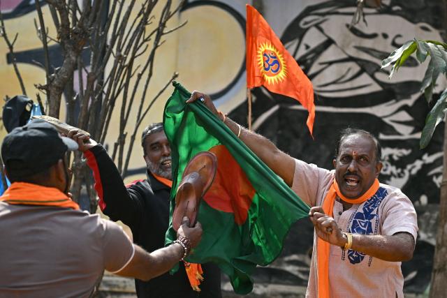 TOPSHOT - Hindu Rashtra Coordination Committee supporters tear and hit Bangladesh's national flag with sandals next to a saffron religious flag to protest alleged atrocities against Hindus, at the Freedom Park in Bengaluru on December 28, 2025. On December 18, angry mobs in the majority Muslim nation of Bangladesh's capital of Dhaka attacked the offices of Prothom Alo and the Daily Star, torching parts of the buildings and vandalising the premises of the two publications caught up in surging anti-India sentiment in the wake of popular student leader Sharif Osman Hadi's death. The violence also saw Hindu garment worker Dipu Chandra Das killed following allegations of blasphemy. (Photo by Idrees MOHAMMED / AFP)
