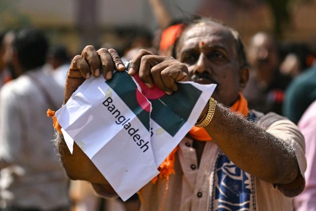 A Hindu Rashtra Coordination Committee supporter tears a paper featuring Bangladesh's national flag to protest alleged atrocities against Hindus, at the Freedom Park in Bengaluru on December 28, 2025. Angry mobs in Dhaka, capital of majority Muslim nation Bangladesh attacked the offices of Prothom Alo and the Daily Star on December 18, torching parts of the buildings and vandalising the premises of the two publications caught up in surging anti-India sentiment in the wake of popular student leader Sharif Osman Hadi's death. The violence also saw Hindu garment worker Dipu Chandra Das killed following allegations of blasphemy. (Photo by Idrees MOHAMMED / AFP)