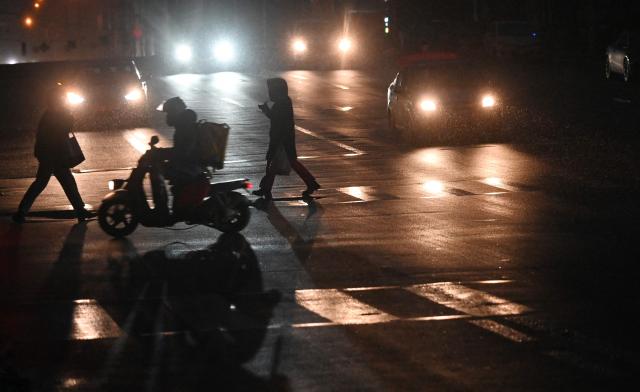 Pedestrians cross a non-illuminated street during a power outage in Kyiv on December 27, 2025, following Russian missile and drone attacks on Ukrainian energy infrastructure amid the Russian invasion of Ukraine. (Photo by Sergei SUPINSKY / AFP)