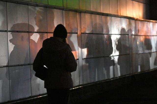 This photograph shows shadows of walking people on a wall lighted by vehicles headlights driving down a non-illuminated street during a power outage in Kyiv on December 27, 2025, following Russian missile and drone attacks on Ukrainian energy infrastructure amid the Russian invasion of Ukraine. (Photo by Sergei SUPINSKY / AFP)