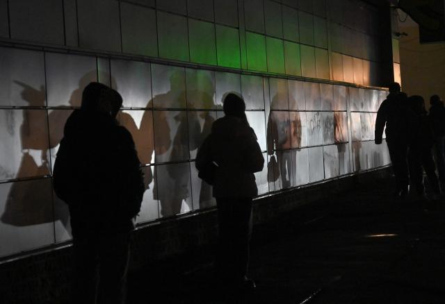 This photograph shows shadows of walking people on a wall lighted by vehicles headlights driving down a non-illuminated street during a power outage in Kyiv on December 27, 2025, following Russian missile and drone attacks on Ukrainian energy infrastructure amid the Russian invasion of Ukraine. (Photo by Sergei SUPINSKY / AFP)