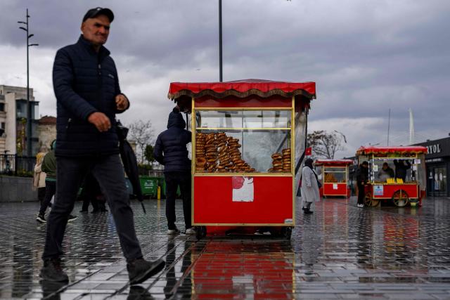 A street vendor sells traditional Turkish bagel "Simit" as he waits for customers, in the Eminonu district of Istanbul, on December 27, 2025. Simit roams the streets of Turkey as surely as cats. But the price of this small, round, ring-shaped bread, studded with sesame seeds, is also a stark indicator of the dizzying price increases. (Photo by Yasin AKGUL / AFP)