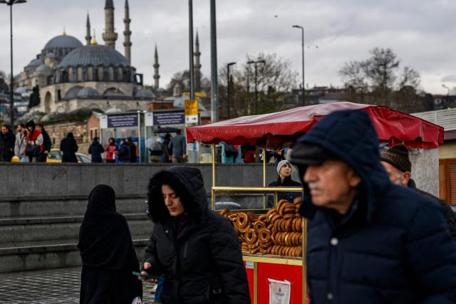 People walk past the counter of a traditional Turkish bagel "Simit" street vendor, in the Eminonu district of Istanbul, on December 27, 2025. Simit roams the streets of Turkey as surely as cats. But the price of this small, round, ring-shaped bread, studded with sesame seeds, is also a stark indicator of the dizzying price increases. (Photo by Yasin AKGUL / AFP)
