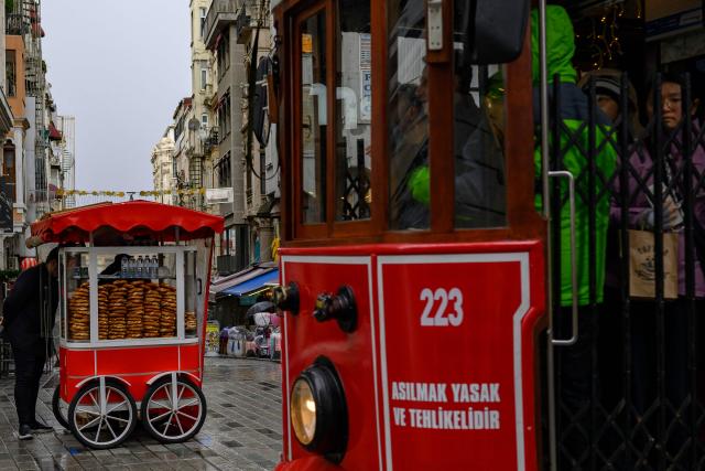 A street vendor sells traditional Turkish bagels "Simit", as he waits for customers at Taksim Square, in Istanbul, on December 27, 2025. Simit roams the streets of Turkey as surely as cats. But the price of this small, round, ring-shaped bread, studded with sesame seeds, is also a stark indicator of the dizzying price increases. (Photo by Yasin AKGUL / AFP)