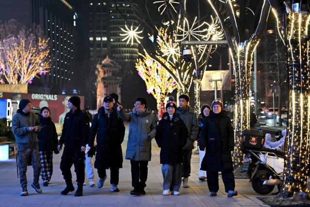 People walk past a shopping mall in Beijing on December 28, 2025. (Photo by ADEK BERRY / AFP)